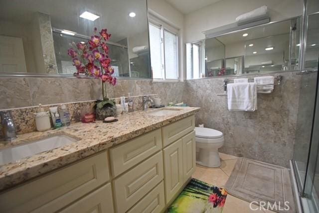 bathroom with tile patterned floors, an enclosed shower, toilet, vanity, and tile walls