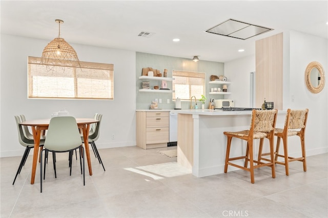 kitchen featuring hanging light fixtures, sink, dishwasher, a breakfast bar, and light brown cabinetry