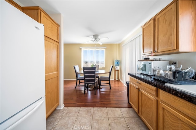 kitchen featuring dark stone counters, light wood-type flooring, white appliances, and ceiling fan