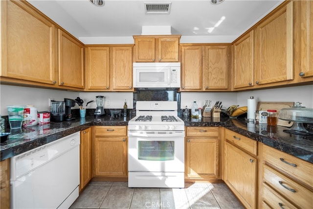 kitchen featuring dark stone countertops, light tile patterned flooring, and white appliances