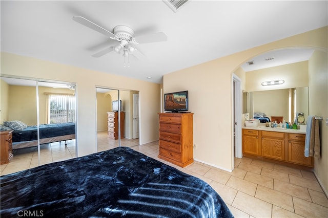 bedroom with sink, ceiling fan, connected bathroom, light tile patterned floors, and two closets