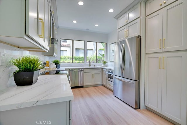 kitchen with a sink, light wood-type flooring, recessed lighting, light stone countertops, and appliances with stainless steel finishes