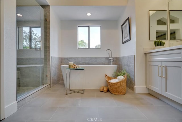 full bathroom with tile walls, a freestanding tub, vanity, and a healthy amount of sunlight