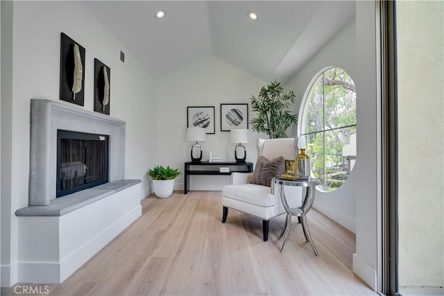 living area featuring wood finished floors, a fireplace with raised hearth, baseboards, lofted ceiling, and visible vents
