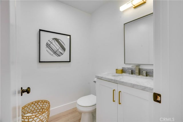 half bathroom featuring baseboards, wood finished floors, toilet, and vanity