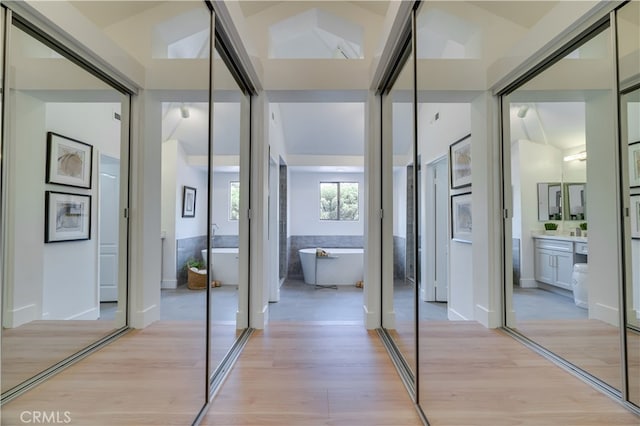 corridor featuring light wood-type flooring and vaulted ceiling