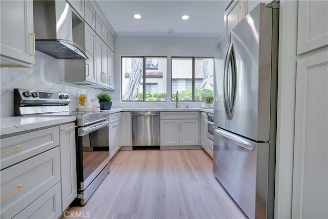 kitchen featuring a sink, light wood-style floors, wall chimney exhaust hood, appliances with stainless steel finishes, and recessed lighting