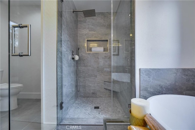 full bathroom featuring a soaking tub, toilet, a stall shower, baseboards, and tile patterned flooring