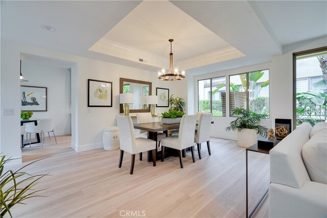 dining area featuring a tray ceiling, a chandelier, and light hardwood / wood-style flooring