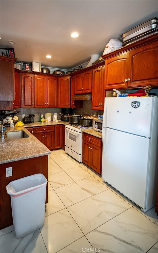 kitchen featuring light stone countertops, a sink, white appliances, tasteful backsplash, and under cabinet range hood
