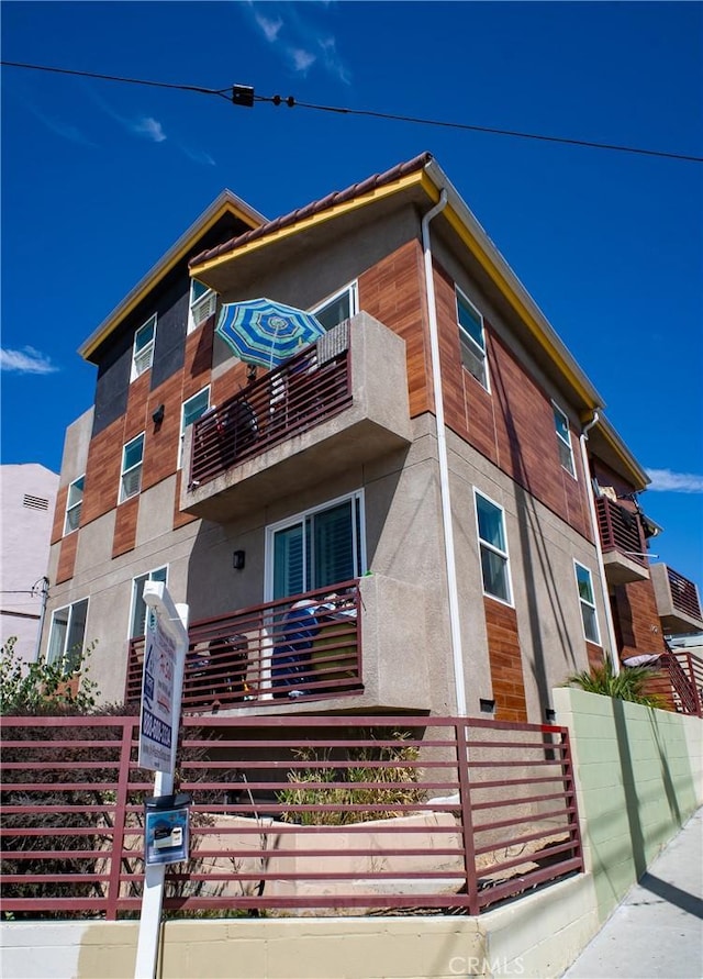view of front of house with fence private yard, stucco siding, and a balcony