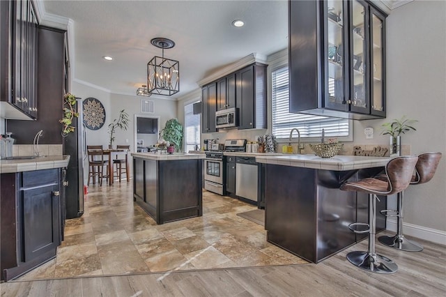 kitchen with decorative light fixtures, tile countertops, a kitchen breakfast bar, stainless steel appliances, and ornamental molding