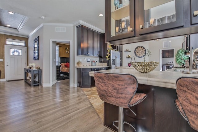 kitchen with light wood-type flooring, stainless steel fridge, a breakfast bar area, ornamental molding, and dark brown cabinets