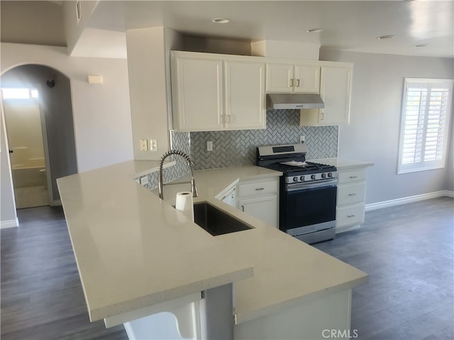 kitchen featuring white cabinets, tasteful backsplash, sink, kitchen peninsula, and stainless steel gas range oven