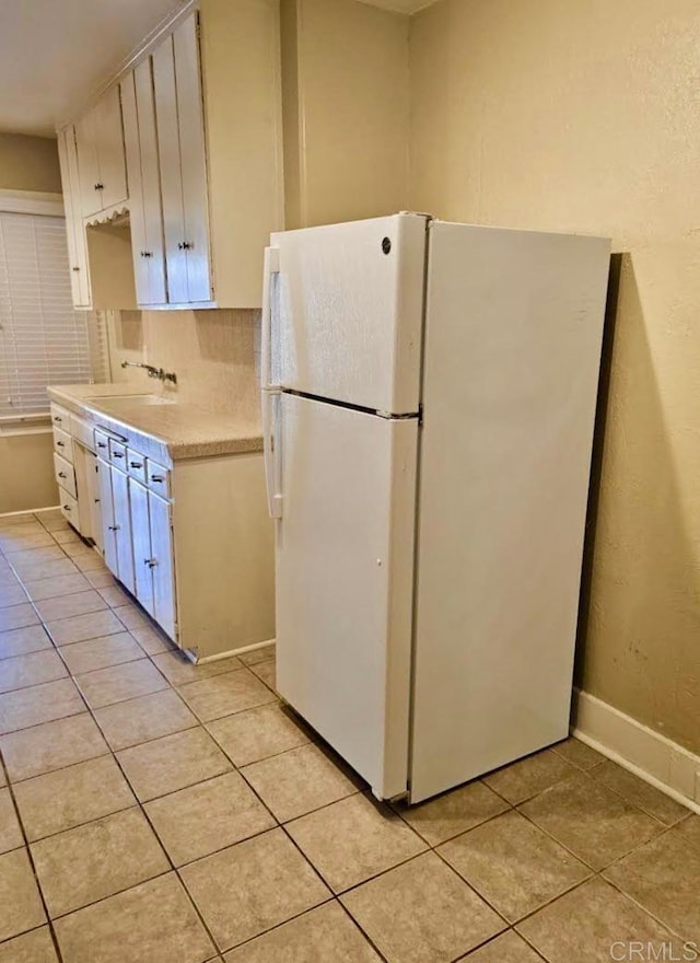 kitchen with light tile patterned floors, sink, white fridge, and white cabinetry