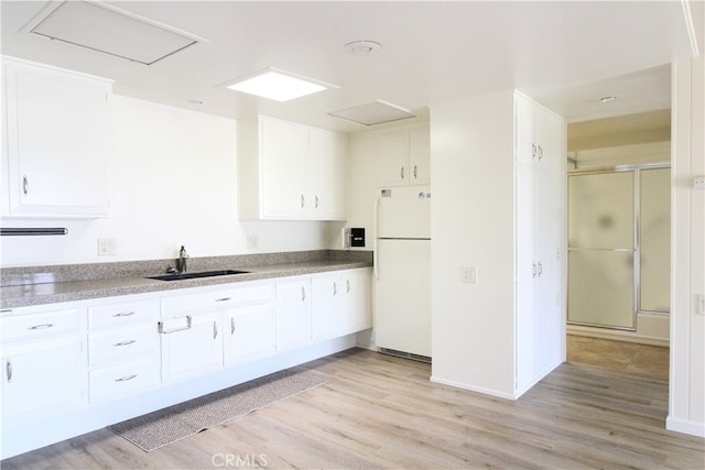 kitchen with white refrigerator, light wood-type flooring, sink, and white cabinetry