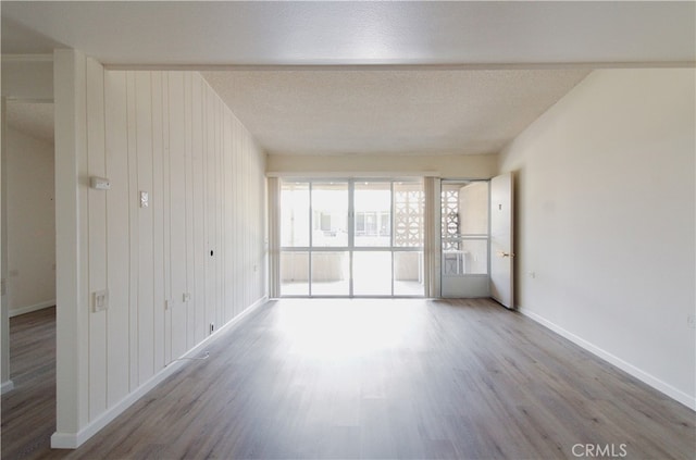 spare room featuring a textured ceiling, light wood-type flooring, and wood walls