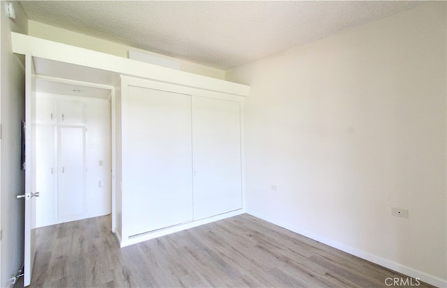 unfurnished bedroom with a textured ceiling, a closet, and light hardwood / wood-style floors