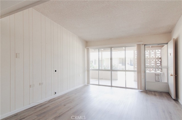 empty room with wooden walls, light wood-type flooring, and a textured ceiling