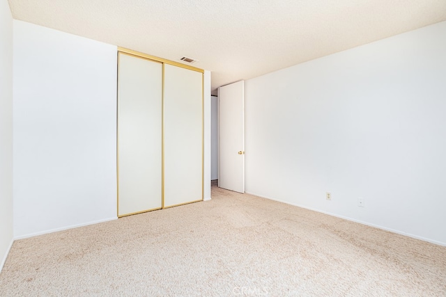 unfurnished bedroom with a closet, a textured ceiling, and light colored carpet