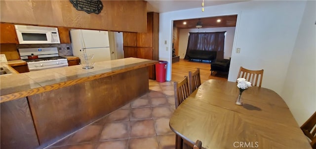 kitchen with tasteful backsplash, tile counters, kitchen peninsula, dark tile patterned floors, and white appliances