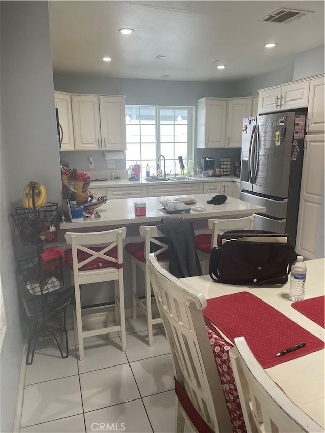 kitchen featuring a kitchen breakfast bar, sink, white cabinets, stainless steel fridge with ice dispenser, and light tile patterned flooring