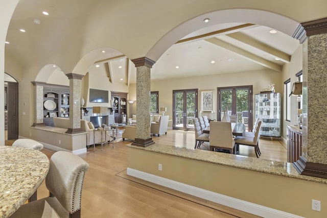 dining space featuring beamed ceiling, a towering ceiling, decorative columns, and light wood-type flooring