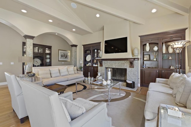 living room with a high end fireplace, light wood-type flooring, lofted ceiling with beams, and ornate columns