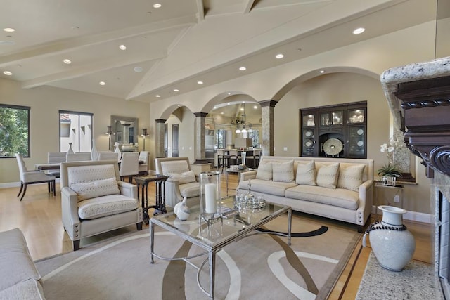 living room featuring hardwood / wood-style flooring, beam ceiling, high vaulted ceiling, and ornate columns