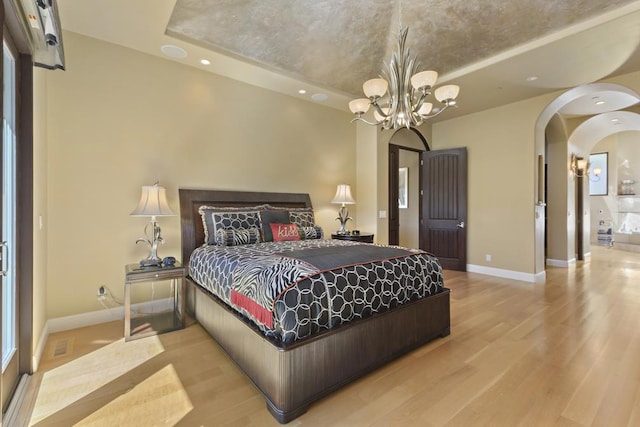 bedroom with an inviting chandelier, light hardwood / wood-style floors, and a tray ceiling