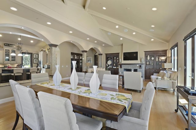 dining room with decorative columns, high vaulted ceiling, beam ceiling, and light hardwood / wood-style flooring