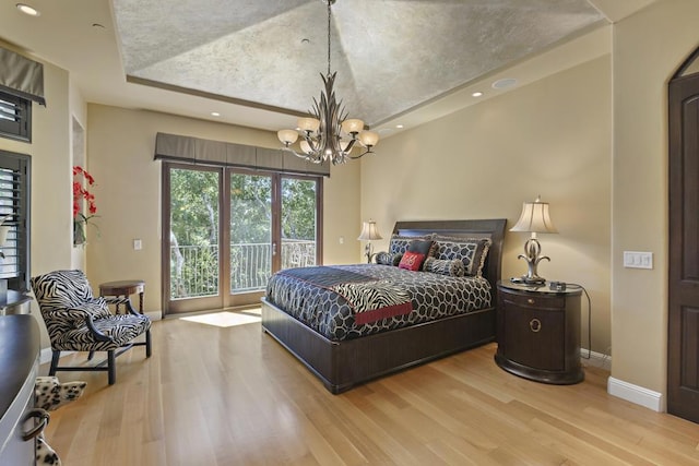 bedroom with an inviting chandelier, a tray ceiling, hardwood / wood-style floors, and access to outside