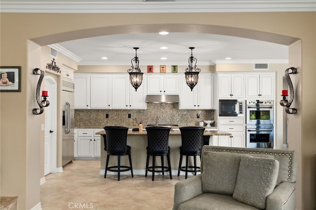 kitchen with white cabinetry, stainless steel appliances, decorative light fixtures, a breakfast bar, and a center island with sink