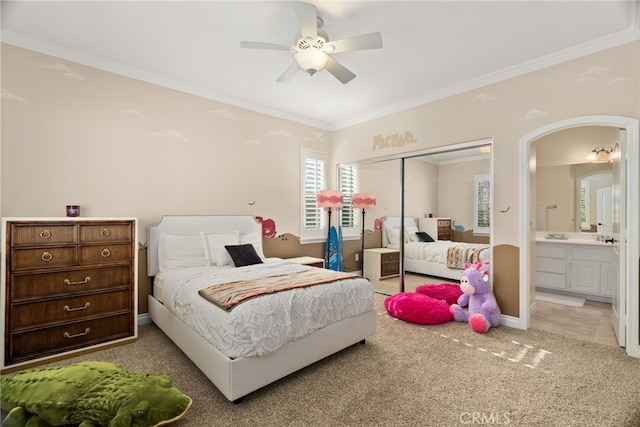 carpeted bedroom with a closet, ceiling fan, connected bathroom, and ornamental molding