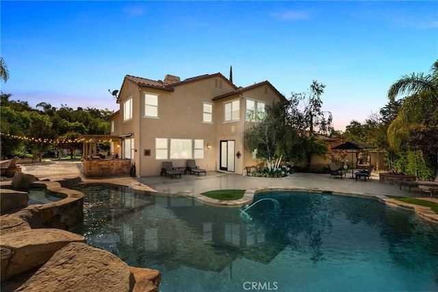 back house at dusk with a patio area, a pool with hot tub, and a bar