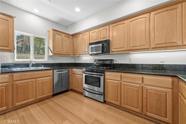 kitchen with sink, light hardwood / wood-style flooring, dark stone countertops, and stainless steel appliances