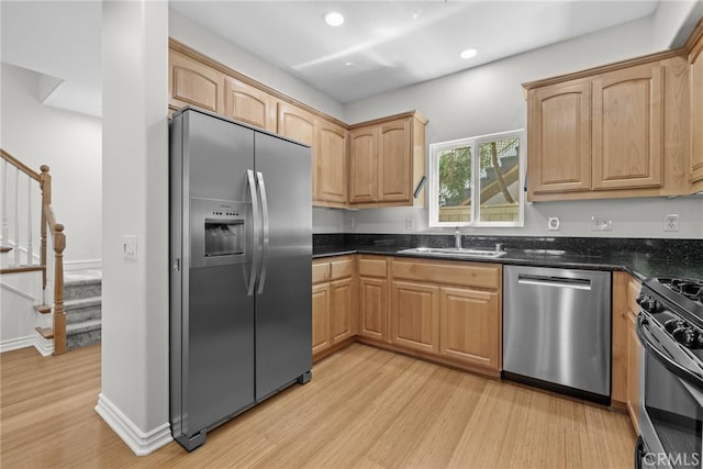 kitchen featuring light brown cabinets, light hardwood / wood-style flooring, appliances with stainless steel finishes, sink, and dark stone countertops