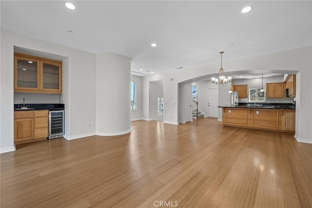 unfurnished living room featuring light wood-type flooring, a notable chandelier, wine cooler, and indoor wet bar