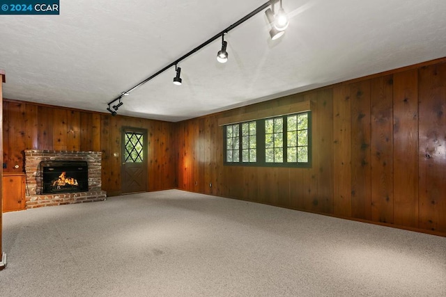 unfurnished living room with a wealth of natural light, carpet floors, track lighting, and a brick fireplace