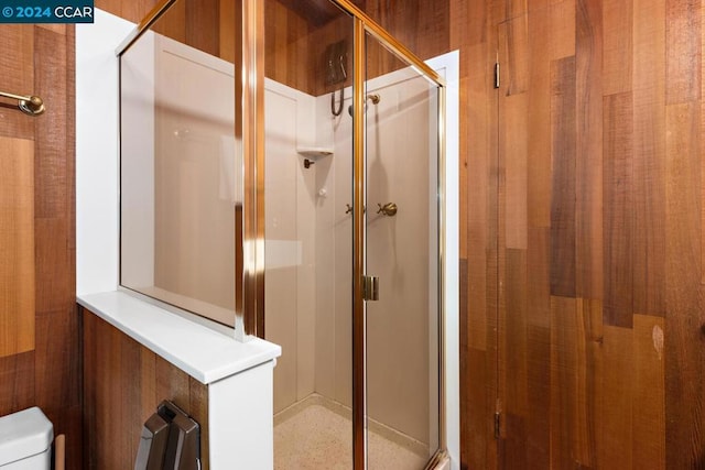 bathroom with toilet, an enclosed shower, and wooden walls