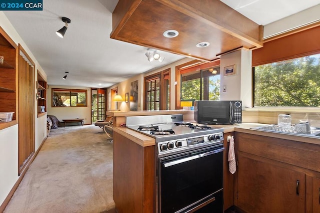 kitchen featuring gas stove, kitchen peninsula, and light colored carpet