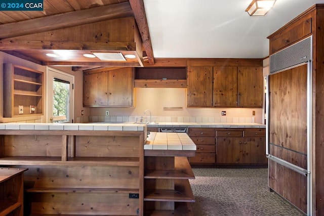 kitchen featuring wood ceiling, vaulted ceiling, dark colored carpet, paneled built in fridge, and tile counters