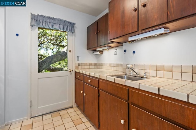 kitchen with tile countertops, backsplash, light tile patterned floors, and sink