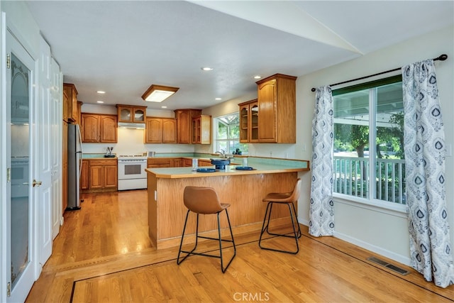 kitchen with a kitchen bar, kitchen peninsula, a healthy amount of sunlight, and white stove