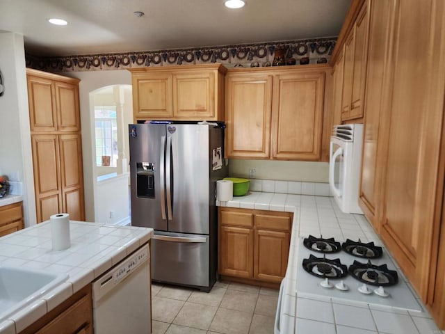 kitchen with tile countertops, white appliances, sink, and light tile patterned floors