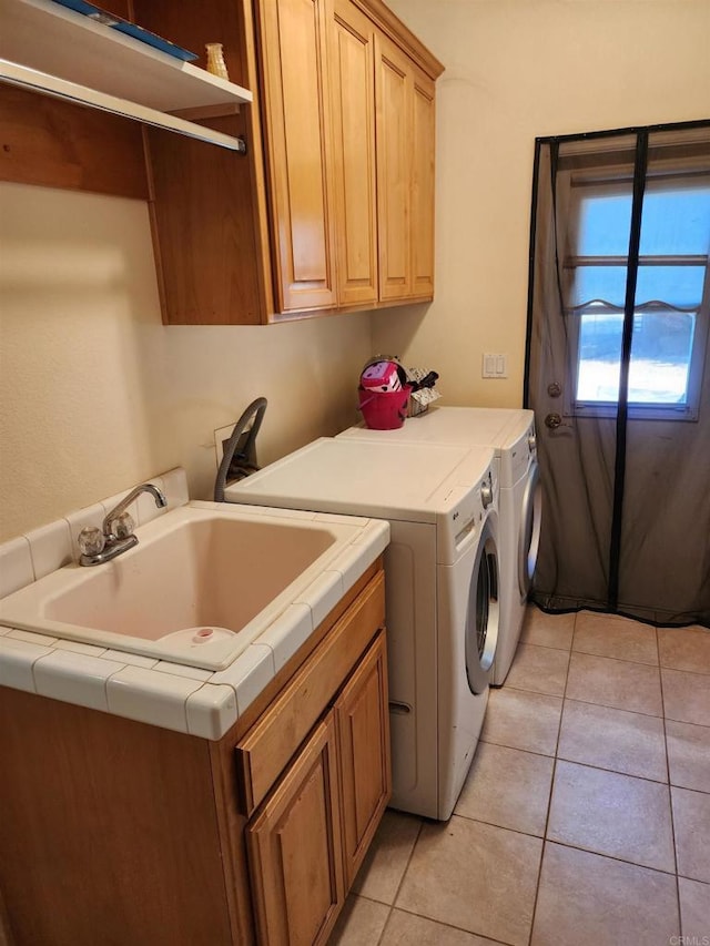 clothes washing area featuring washing machine and dryer, sink, light tile patterned flooring, and cabinets