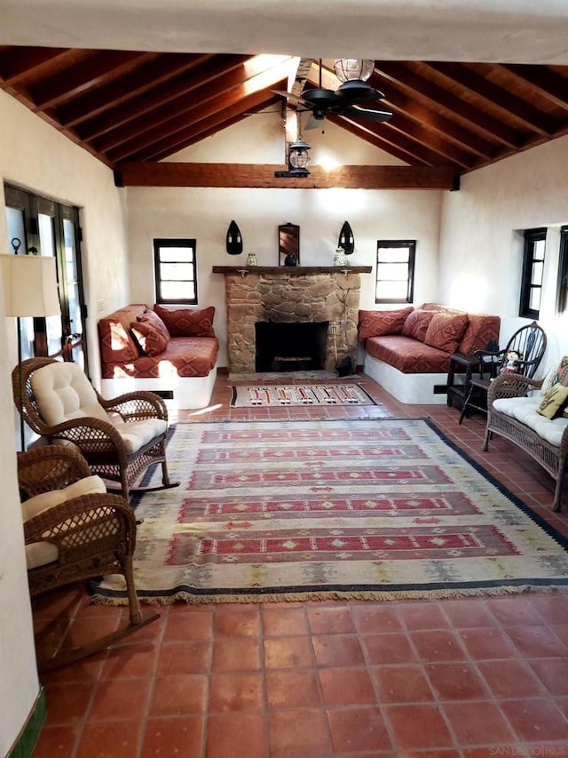 living room featuring lofted ceiling with beams, a stone fireplace, a healthy amount of sunlight, and ceiling fan