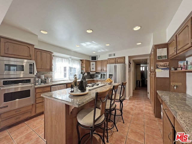 kitchen with backsplash, appliances with stainless steel finishes, a breakfast bar, a kitchen island, and light tile patterned flooring