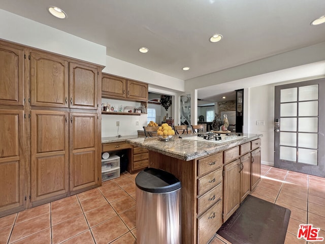 kitchen featuring white gas stovetop, light stone countertops, a center island, and light tile patterned floors