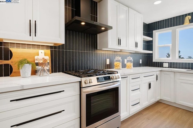 kitchen with light stone countertops, stainless steel stove, white cabinetry, and wall chimney range hood